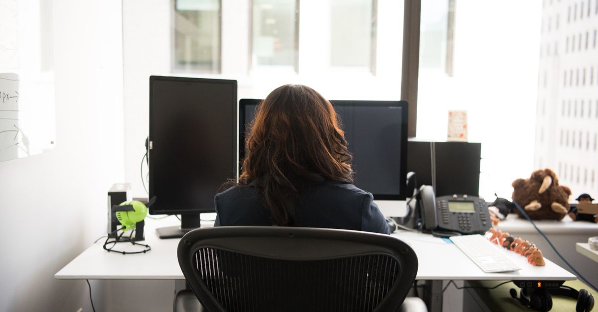 Woman working at a desktop setup in a modern office with technology and city view.